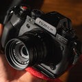 Main tenant un appareil Fujifilm avec une étiquette discrète, bracelet rouge en dessous