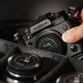 Fujifilm X-T5 avec une étiquette discrète, posé dans un sac photo rembourré, une main s’approchant pour le saisir