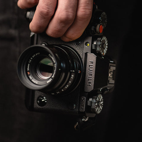 Appareil Fujifilm tenu d’une main sur fond sombre, étiquette discrète sur le boîtier du viseur